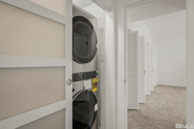 laundry area with light colored carpet, stacked washer / dryer, and brick wall