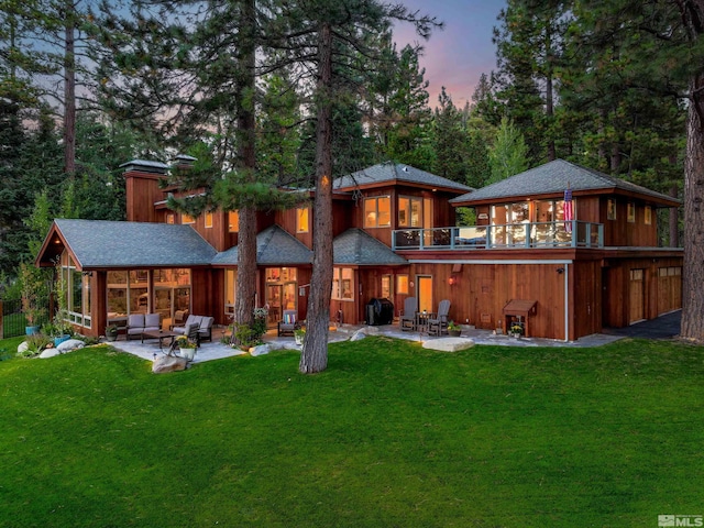 back house at dusk featuring a balcony, an outdoor living space, a yard, and a patio area