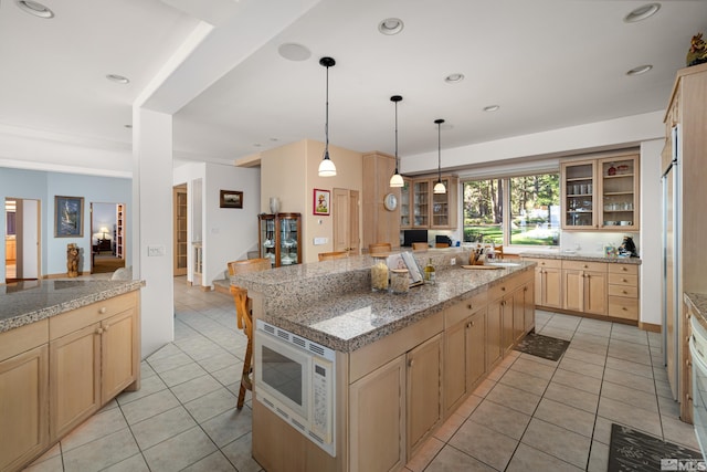 kitchen featuring light tile patterned floors, white microwave, a kitchen island, and light brown cabinets