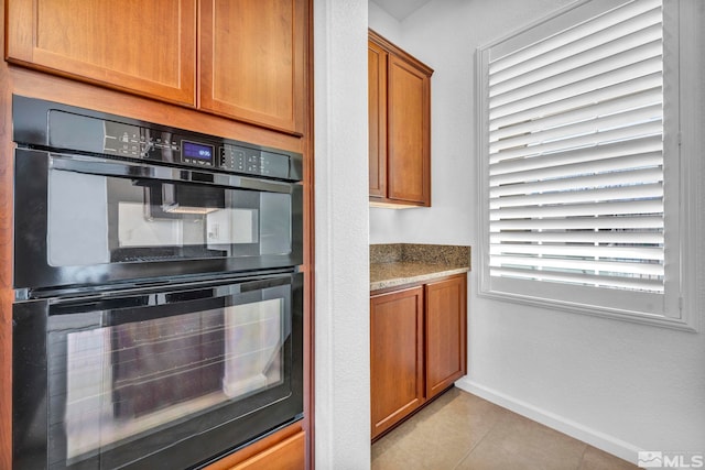 kitchen with black double oven, light stone countertops, and light tile patterned floors