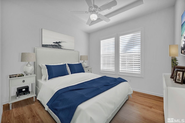 bedroom with a raised ceiling, hardwood / wood-style flooring, and ceiling fan