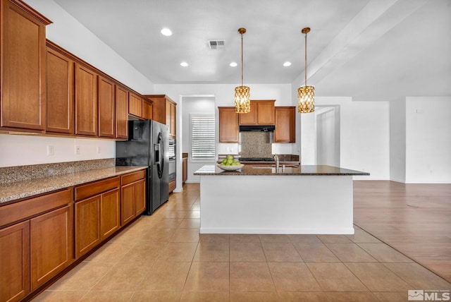 kitchen featuring light tile patterned floors, decorative light fixtures, black fridge with ice dispenser, and a center island with sink