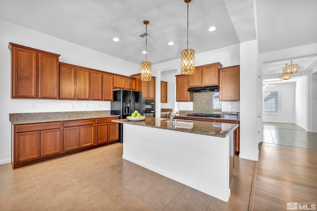 kitchen featuring sink, hanging light fixtures, an island with sink, dark stone counters, and black appliances