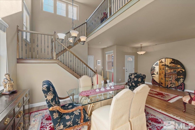 dining space with a towering ceiling, wood-type flooring, and a notable chandelier