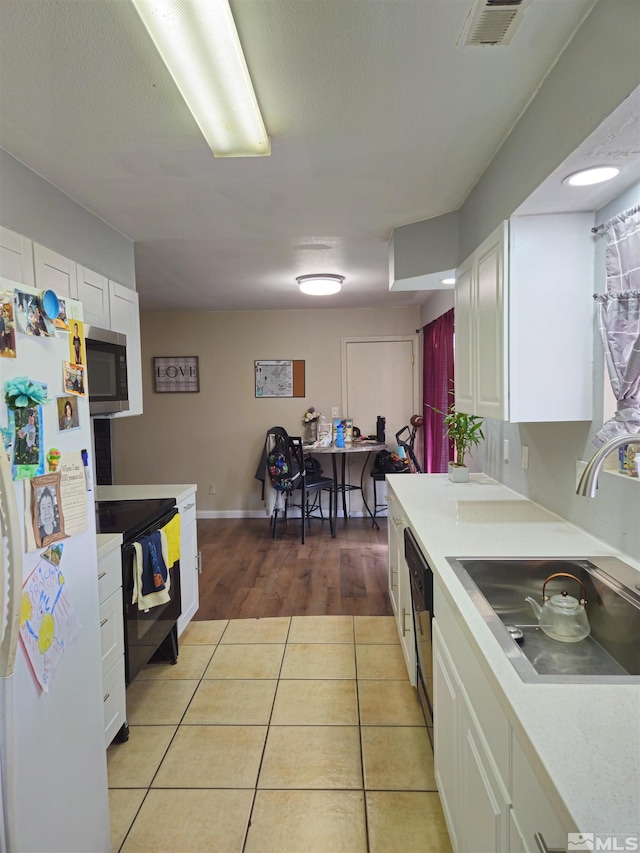 kitchen with sink, white cabinetry, black range with electric stovetop, white refrigerator, and light tile patterned flooring