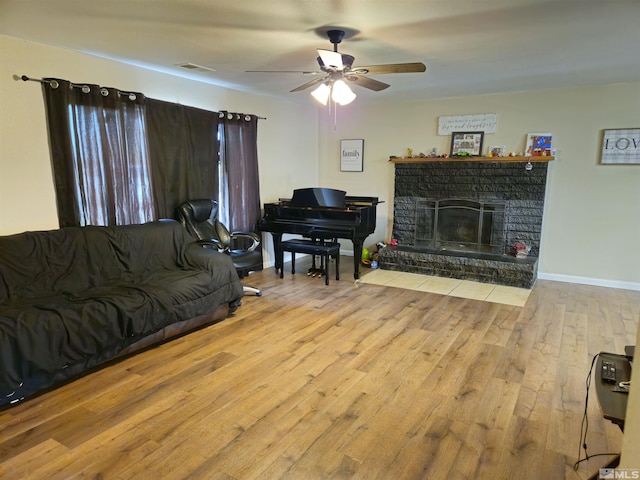 living room with a fireplace, ceiling fan, and light wood-type flooring