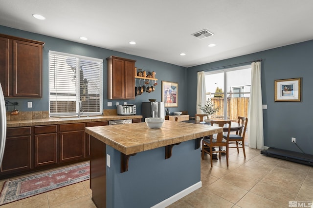 kitchen with dishwasher, a kitchen breakfast bar, a center island, light tile patterned flooring, and tile countertops