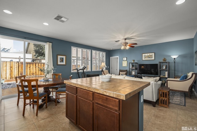 kitchen with ceiling fan, tile counters, a center island, and light tile patterned floors