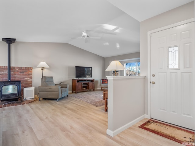 entrance foyer featuring light wood-type flooring, ceiling fan, vaulted ceiling, and a wood stove