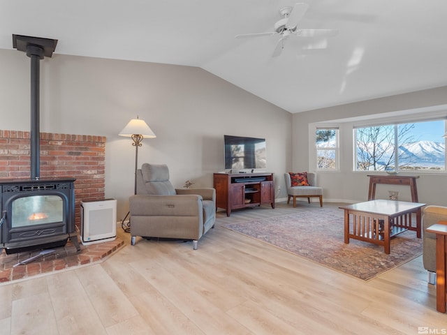 living room with ceiling fan, light wood-type flooring, vaulted ceiling, and a wood stove