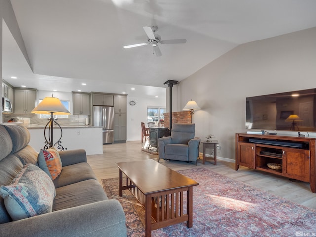 living room with vaulted ceiling, a wood stove, ceiling fan, and light hardwood / wood-style floors