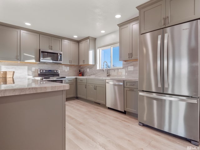 kitchen featuring sink, light hardwood / wood-style flooring, backsplash, stainless steel appliances, and light stone countertops