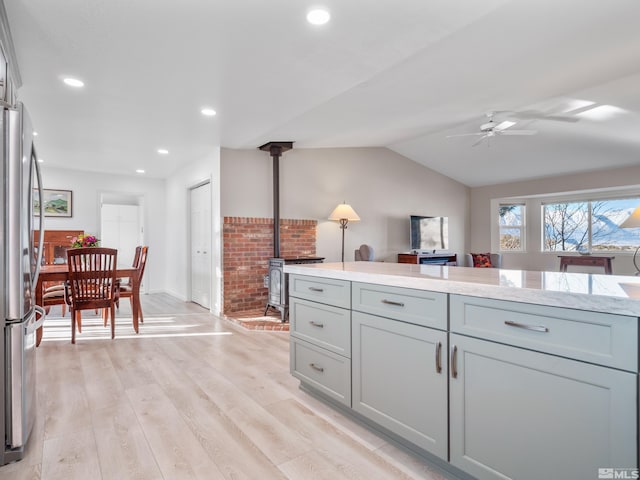 kitchen with gray cabinetry, a wood stove, stainless steel fridge, ceiling fan, and light hardwood / wood-style floors