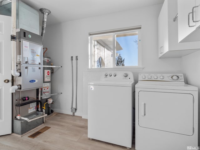 laundry room featuring separate washer and dryer, strapped water heater, light hardwood / wood-style floors, and cabinets