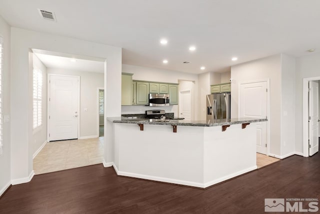 kitchen featuring appliances with stainless steel finishes, wood-type flooring, dark stone counters, green cabinets, and kitchen peninsula