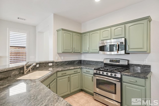 kitchen featuring stainless steel appliances, sink, green cabinets, and dark stone counters