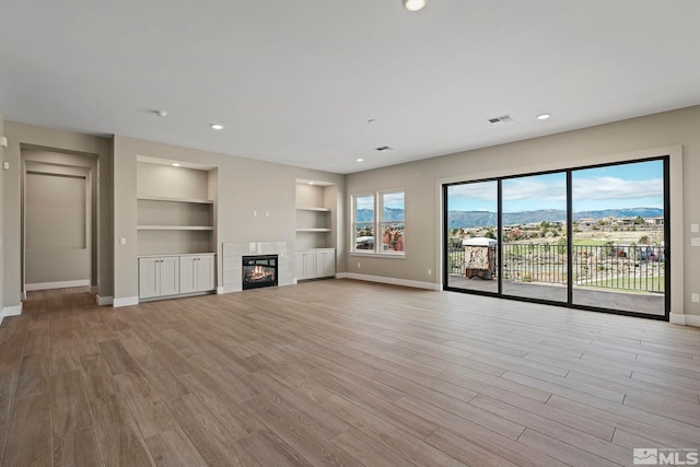 unfurnished living room with a mountain view, light hardwood / wood-style floors, built in shelves, and a tiled fireplace