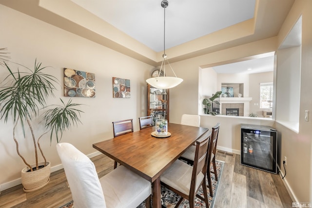 dining area with wood-type flooring, a tray ceiling, a tiled fireplace, and beverage cooler