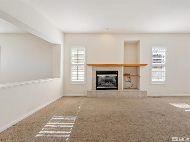 unfurnished living room featuring carpet, a tile fireplace, and a wealth of natural light