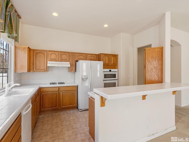 kitchen with a breakfast bar area, sink, tile counters, and white appliances