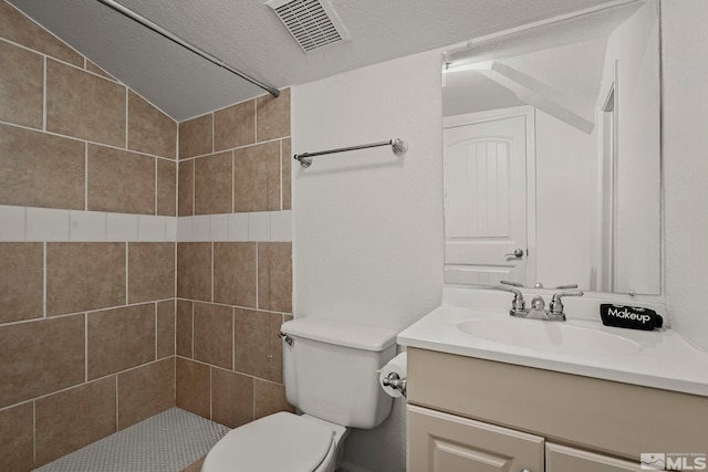bathroom with lofted ceiling, vanity, toilet, and a tile shower