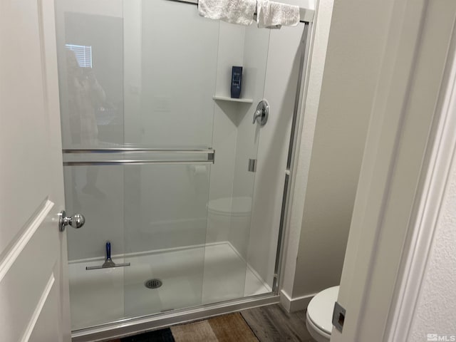 bathroom with wood-type flooring, a shower with shower door, and toilet