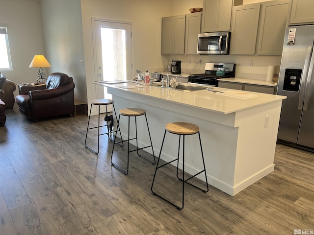 kitchen featuring stainless steel appliances, dark hardwood / wood-style floors, an island with sink, and gray cabinetry