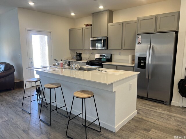 kitchen featuring a kitchen island with sink, gray cabinets, a breakfast bar area, and appliances with stainless steel finishes