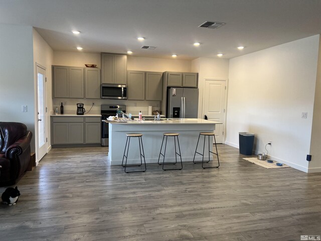 kitchen featuring appliances with stainless steel finishes, gray cabinets, a center island with sink, and a breakfast bar area