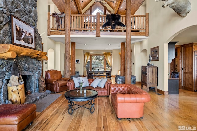 living room featuring a high ceiling, wood-type flooring, and a stone fireplace