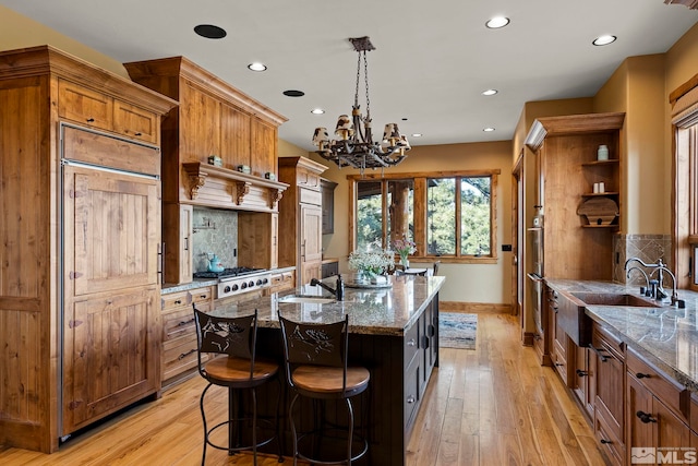 kitchen featuring sink, light stone countertops, an island with sink, decorative light fixtures, and stainless steel gas stovetop