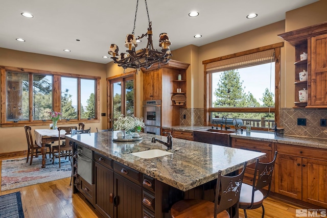 kitchen featuring light hardwood / wood-style floors, light stone countertops, sink, and a center island with sink