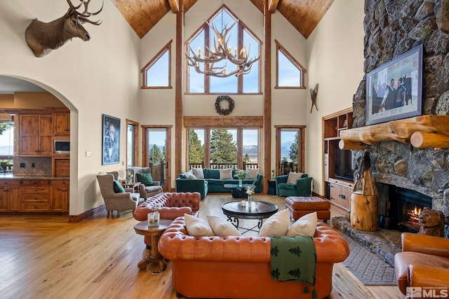 living room with a stone fireplace, wood ceiling, a chandelier, high vaulted ceiling, and light hardwood / wood-style flooring