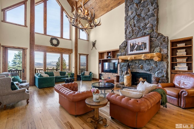 living room with wood ceiling, a stone fireplace, a chandelier, and light wood-type flooring