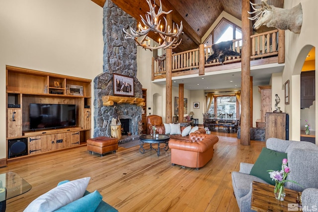 living room with wood ceiling, light hardwood / wood-style flooring, an inviting chandelier, high vaulted ceiling, and a stone fireplace