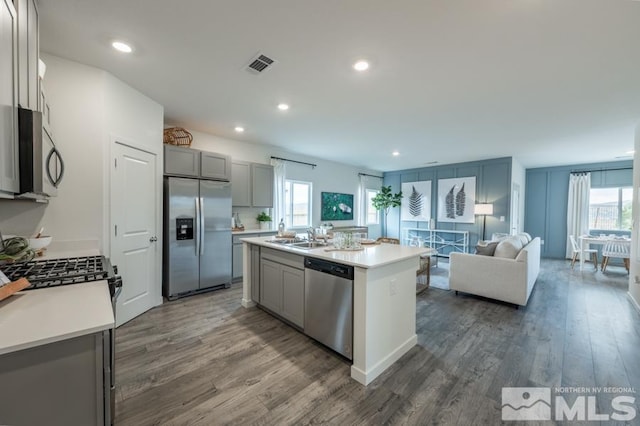 kitchen with stainless steel appliances, an island with sink, gray cabinets, and dark hardwood / wood-style floors