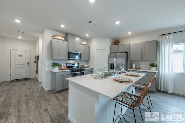 kitchen with appliances with stainless steel finishes, a kitchen island with sink, and gray cabinetry