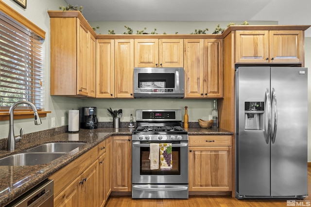 kitchen featuring sink, light hardwood / wood-style flooring, stainless steel appliances, and dark stone counters