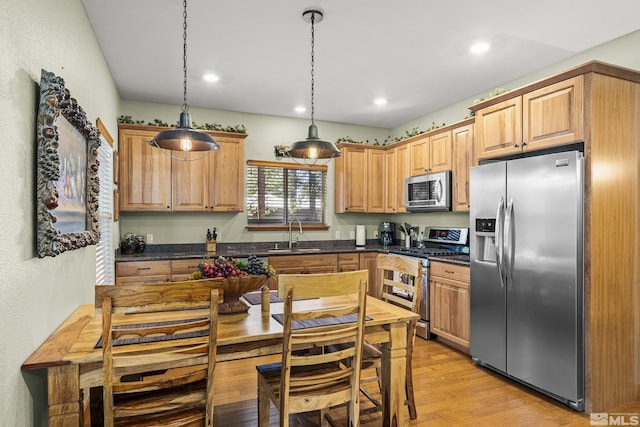 kitchen with stainless steel appliances, sink, light wood-type flooring, and decorative light fixtures