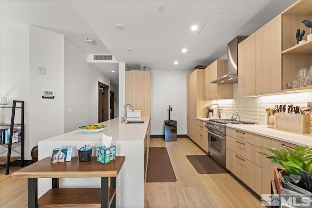 kitchen with sink, high end stainless steel range oven, light brown cabinetry, decorative backsplash, and wall chimney exhaust hood