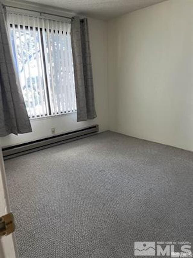 carpeted spare room featuring a baseboard heating unit