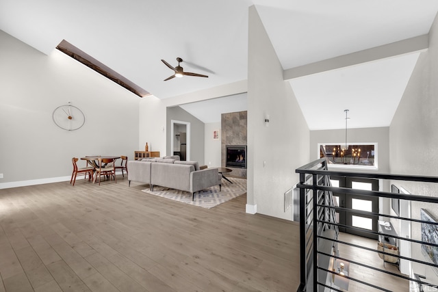 interior space with hardwood / wood-style flooring, high vaulted ceiling, a tiled fireplace, and ceiling fan with notable chandelier