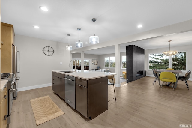 kitchen featuring sink, appliances with stainless steel finishes, an island with sink, pendant lighting, and light hardwood / wood-style floors