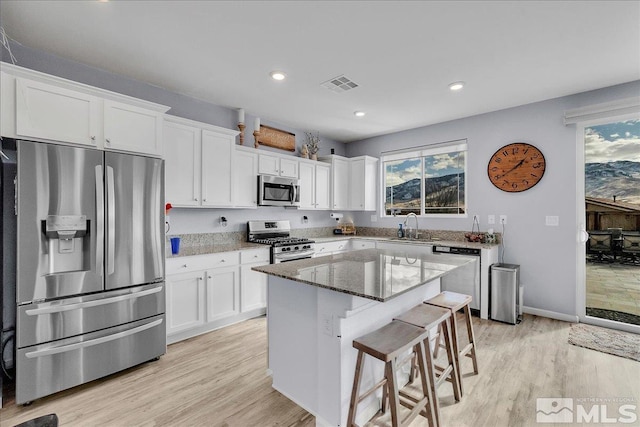 kitchen featuring appliances with stainless steel finishes, white cabinetry, sink, dark stone counters, and a center island