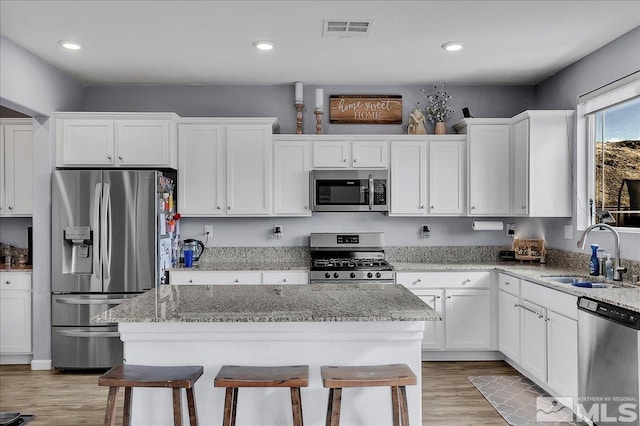 kitchen with sink, light stone countertops, white cabinets, and appliances with stainless steel finishes