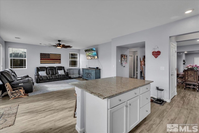 kitchen featuring a kitchen island, white cabinets, ceiling fan, light hardwood / wood-style floors, and light stone countertops