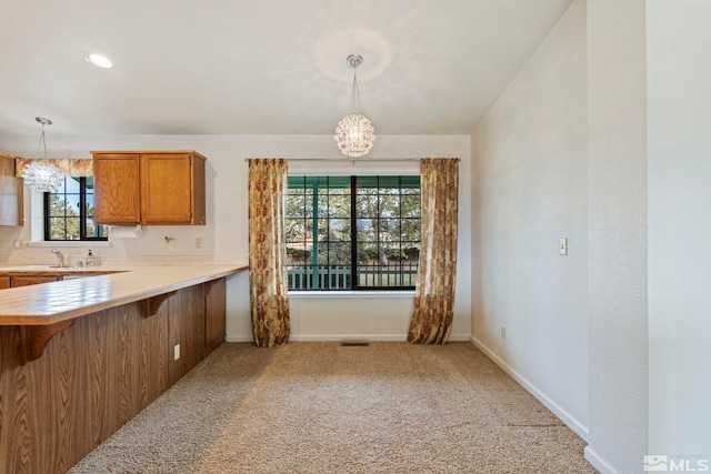 kitchen with a breakfast bar area, hanging light fixtures, kitchen peninsula, a notable chandelier, and light colored carpet