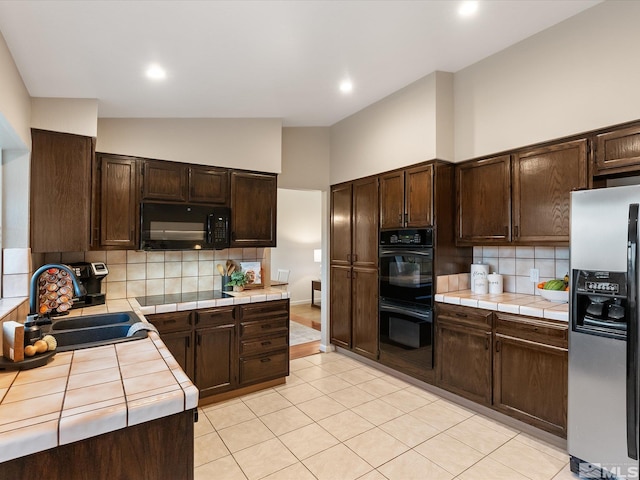 kitchen with tile counters, sink, dark brown cabinets, and black appliances