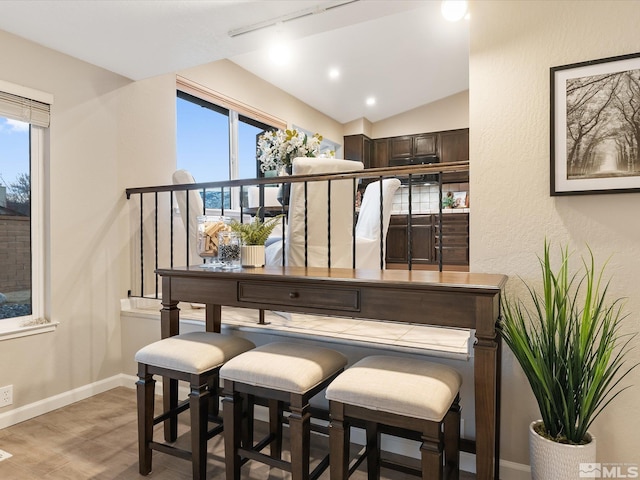 bar featuring lofted ceiling, dark brown cabinetry, track lighting, and light wood-type flooring