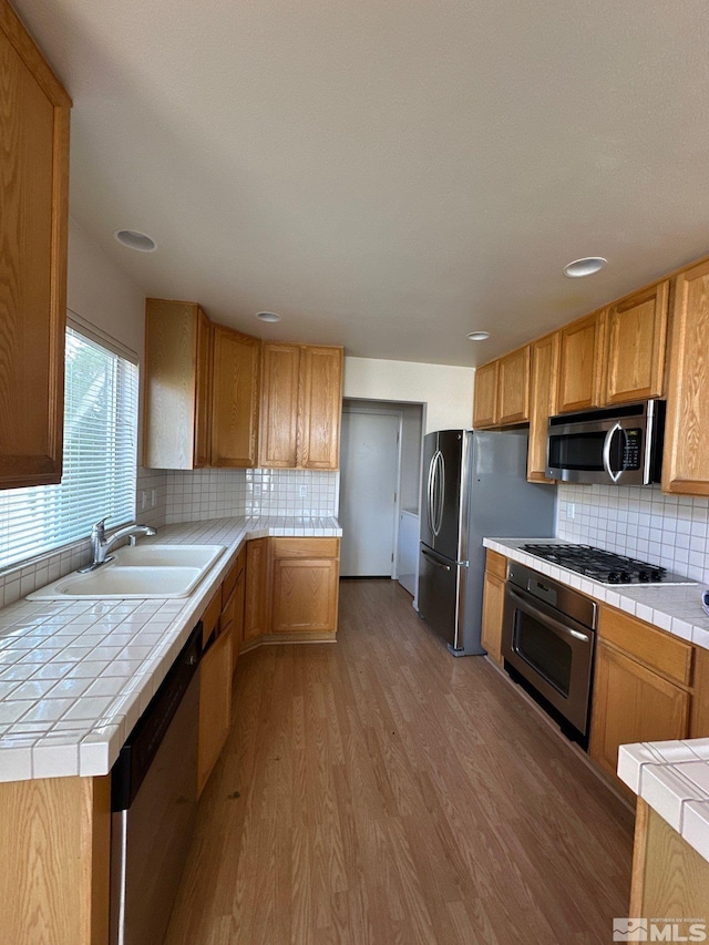 kitchen with stainless steel appliances, backsplash, wood finished floors, tile countertops, and a sink